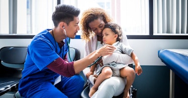 A nurse uses a stethoscope on a child that's sitting in their mother's lap.