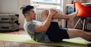 一名男子在家里的瑜伽垫上仰面伸展，把膝盖拉到胸前。