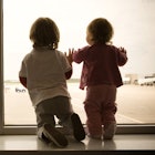 Two children look out the airport window at the airplanes.