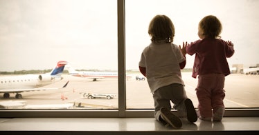 Two children look out the airport window at the airplanes.