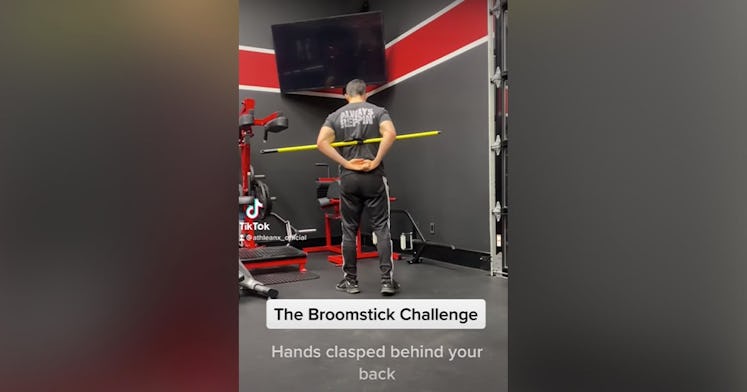 Screenshot of a video of a man with a broomstick under his arms and behind his back as he does the b...