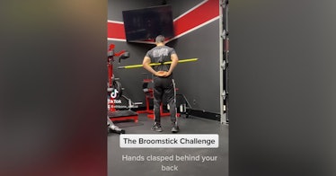 Screenshot of a video of a man with a broomstick under his arms and behind his back as he does the b...
