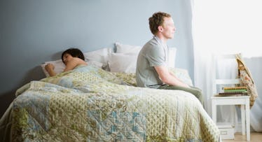 Man sitting up on edge of bed while wife sleeps