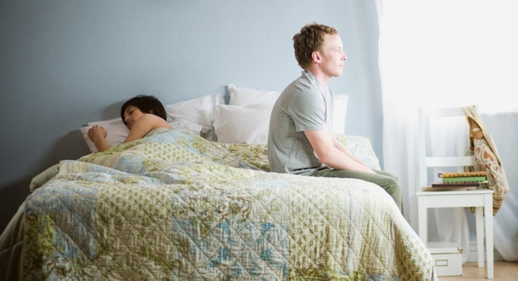 Man sitting up on edge of bed while wife sleeps