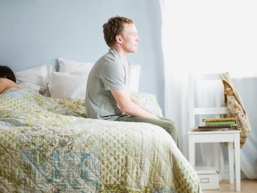 Man sitting up on edge of bed while wife sleeps