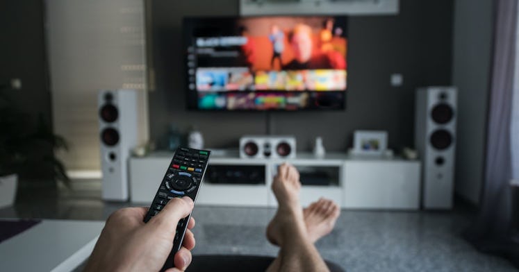 A man holding a remote control and watching HBO Max on TV