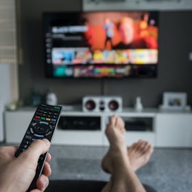 A man holding a remote control and watching HBO Max on TV