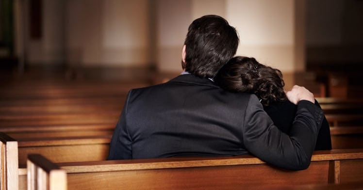 A mother and father sit in a pew in their funeral clothes.