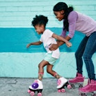 a kid and another kid rollerskate against a blue wall