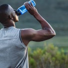 A man drinks water while taking a break from running outside.