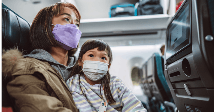 A mother and daughter wear masks on a plane.