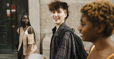 A trans kid carrying a skateboard walks with two friends.