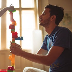 A dad helps his child build a tall tower out of blocks.