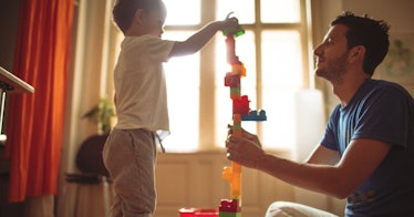 A dad helps his child build a tall tower out of blocks.