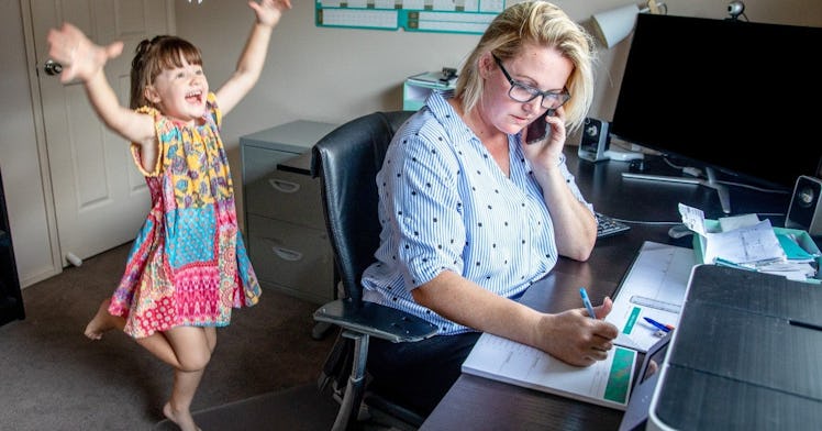 a girl plays behind a mom who is working from home at her desk