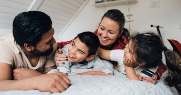 An autistic child lays down with his parents and sister, all looking happy.