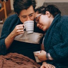 A couple with the flu is holed up together at home, wrapped in blankets and drinking tea.