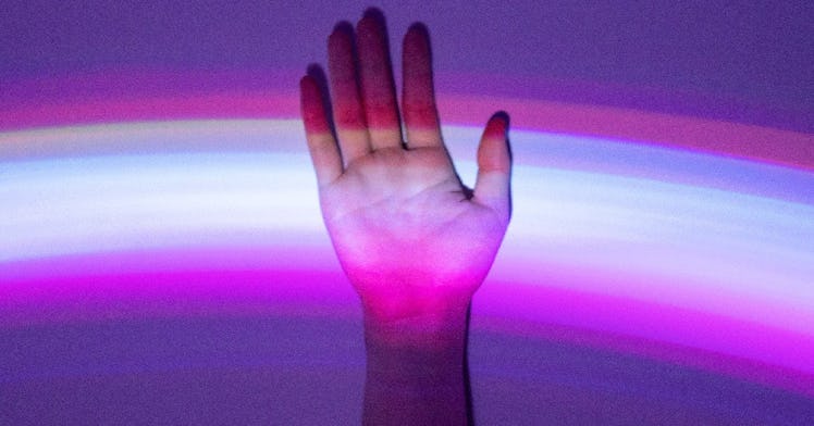 a hand flat against a wall with a trans rainbow lighting it