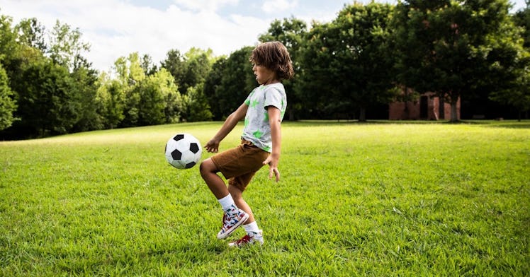 A kid plays in a green park with a soccer ball