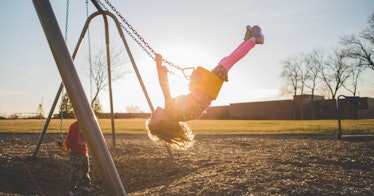 a kid plays on the swings as the sun shines behind them