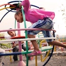 Three kids play on a fast-sprinning play structure in a playground.