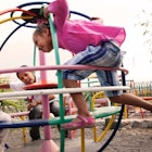 Three kids play on a fast-sprinning play structure in a playground.