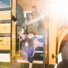 a little kid steps on to a school bus as sun shines on him