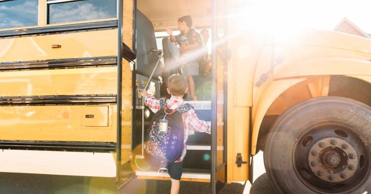 a little kid steps on to a school bus as sun shines on him