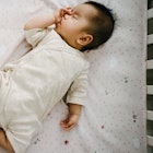 A baby sleeping in a crib, sucking their thumb.