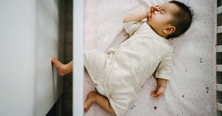 A baby sleeping in a crib, sucking their thumb.
