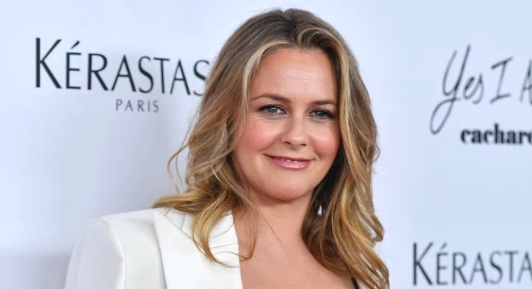 Alicia Silverstone at a red carpet, in a white blazer, sporting wavy hair.