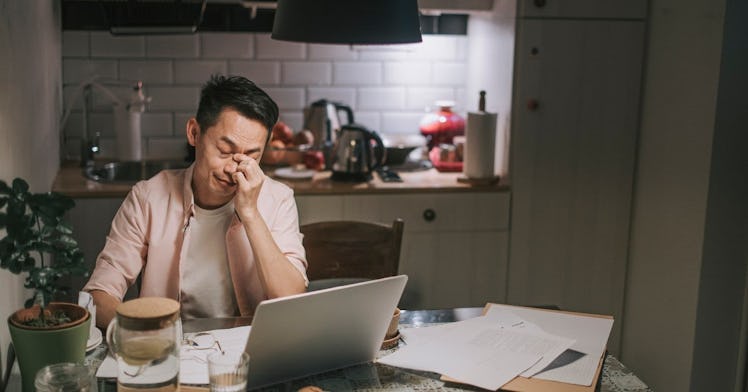 a guy sits, stressed out at his kitchen table looking over finances