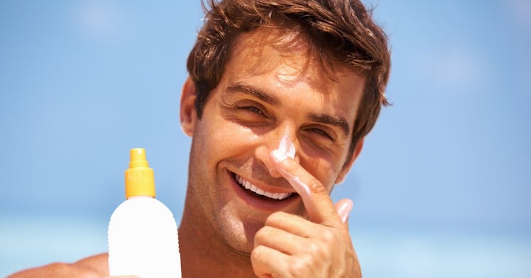 A young man smiling while putting on a sunscreen on his face