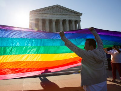 A group of people holding the LGBTQ+ flag in front of the SCOTUS, celebrating the legalization of sa...