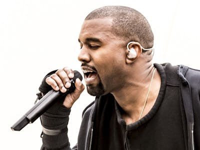 Kanye West performing with a microphone in a black hoodie.