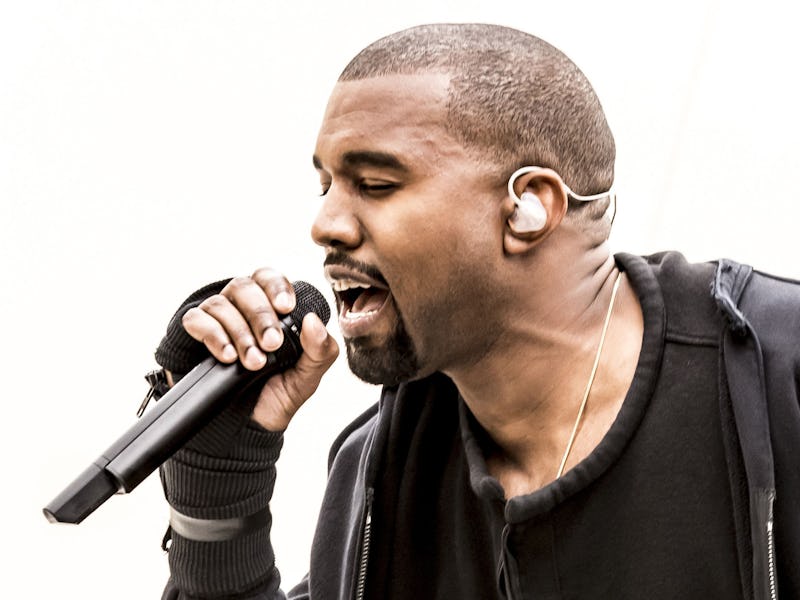 Kanye West performing with a microphone in a black hoodie.