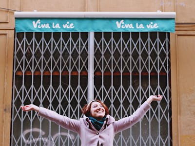 Brown-haired female smiling with raised arms in front of a store