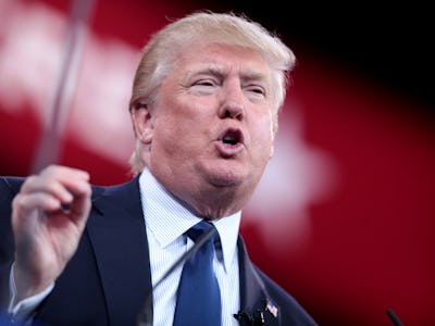 Donald Trump giving a speech in a navy suit, white-blue shirt, and a navy tie