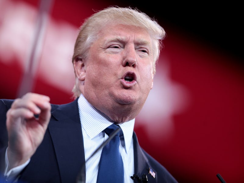 Donald Trump giving a speech in a navy suit, white-blue shirt, and a navy tie