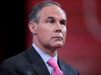 A close-up portrait of Scott Pruitt wearing a black suit, blue shirt, and red tie