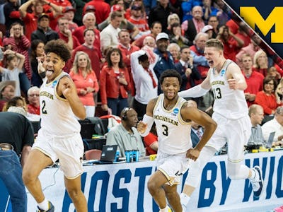 Three players from the Michigan basketball team celebrating a win on the court