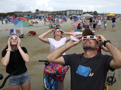 A group of Americans at a beach looking up and watching the eclipse