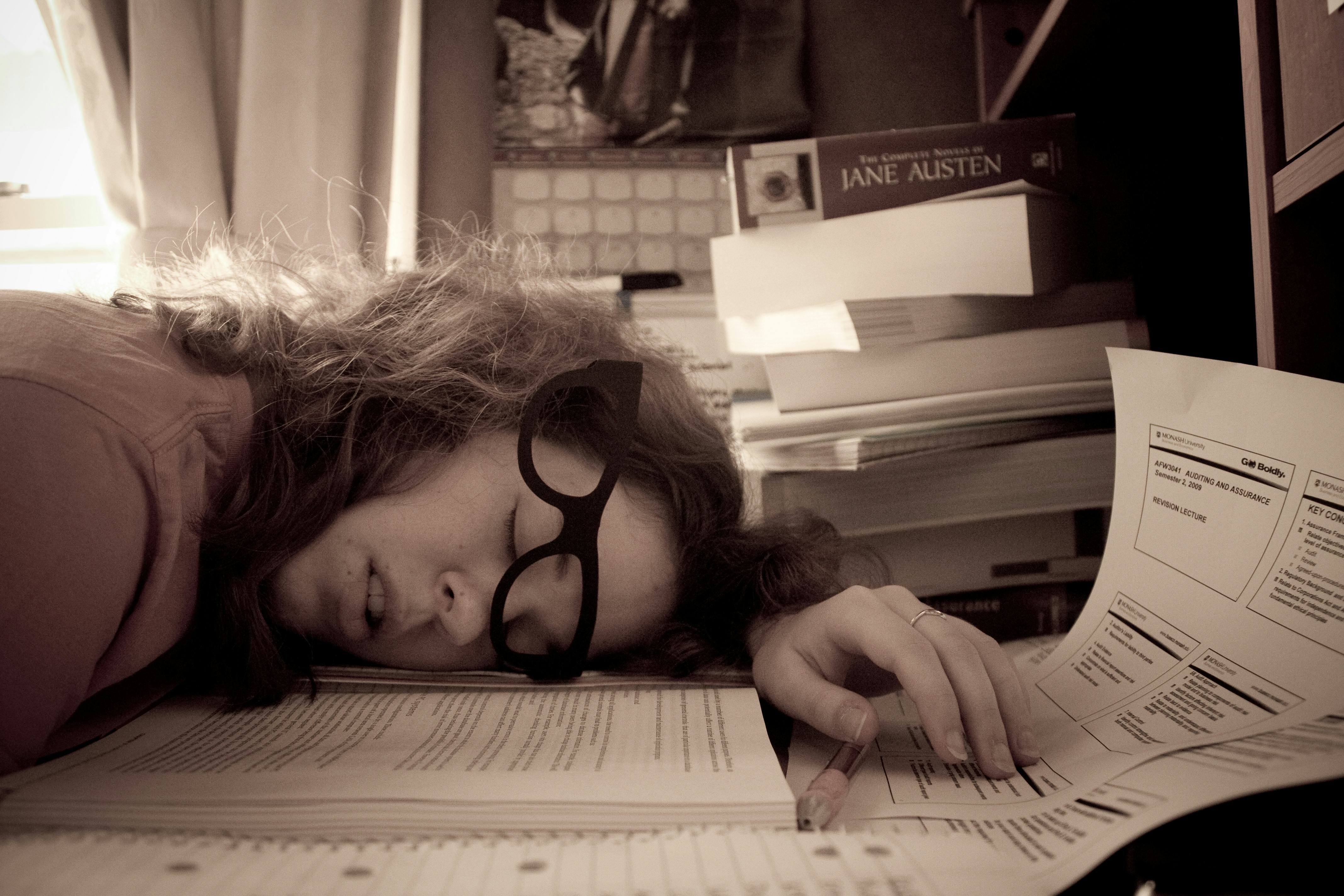 A woman dealing with burnout sleeping on a pile of papers on her desk