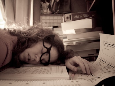 A woman dealing with burnout sleeping on a pile of papers on her desk