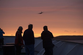 Passengers aboard the Russian research/cruise ship Akademik Ioffe watch a Canadian military aircraft...