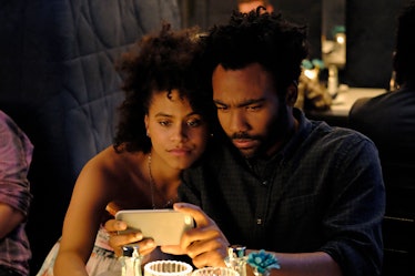 Donald Glover and Zazie Beetz are sitting in a restaurant and looking at a phone.