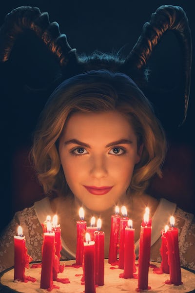 A blonde female smiling and wearing black horns while sitting in front of a cake with red candles 