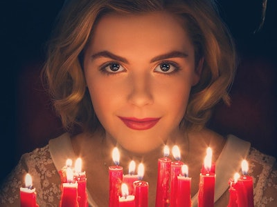 A blonde female smiling and wearing black horns while sitting in front of a cake with red candles 