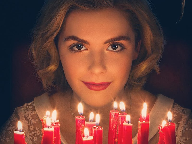 A blonde female smiling and wearing black horns while sitting in front of a cake with red candles