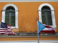 An orange building with the American and Puerto Rican flags waving in front of it